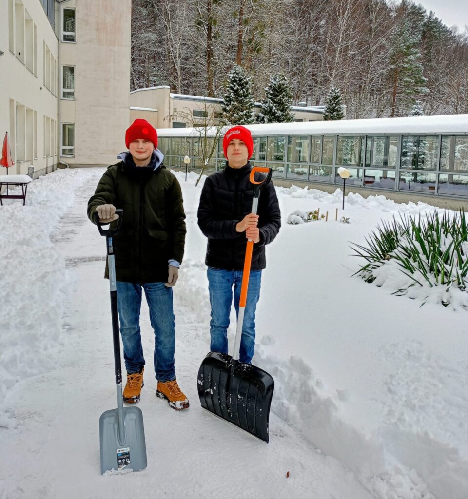 Zbliżenie. Dwóch chłopców w zimowych ubraniach trzymają łopaty do odśnieżania chodników. Chłopcy pozują do zdjęcia.